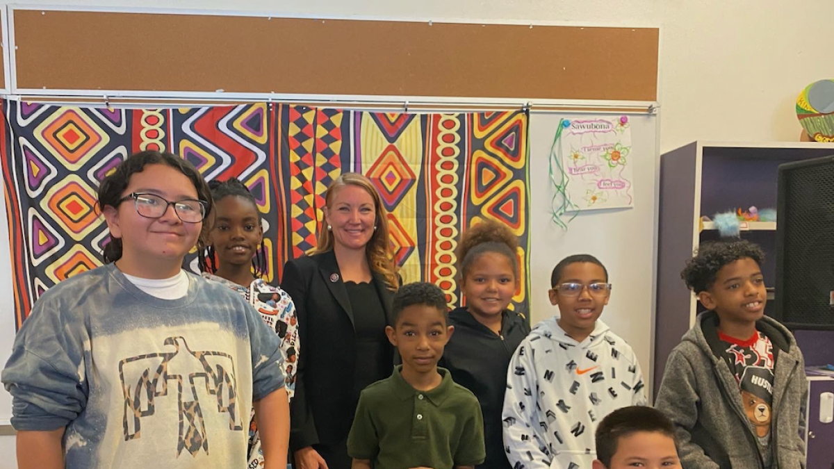 Rep. Stansbury with eight school-age students posing in front of fabric with bright patterns