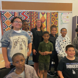 Rep. Stansbury with eight school-age students posing in front of fabric with bright patterns
